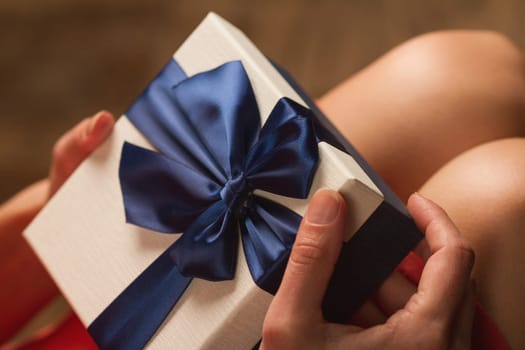 Side view of woman with red dress holding a gift box with blue ribbon on her knees