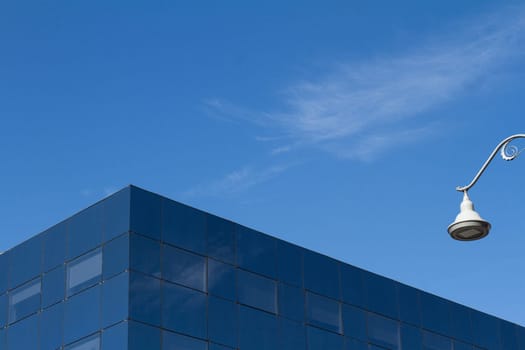 Minimalist photo of a glass office city building detail against a blue sky and a white street light