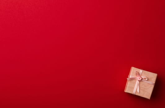 Top view of red background with small pink gift box with white ribbon for greeting cards