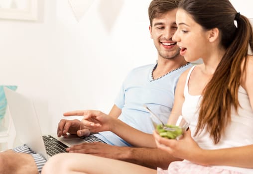 Addicted young man on bed texting while woman looks angry