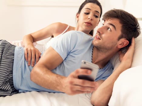 Addicted young man on bed texting while woman looks angry
