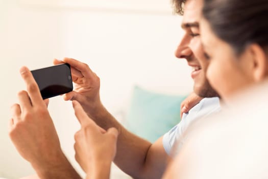 Addicted young man on bed texting while woman looks angry