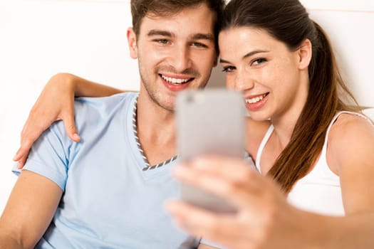 Addicted young man on bed texting while woman looks angry