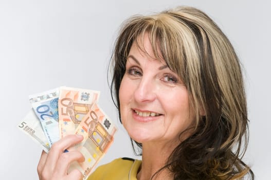 Head-and-shoulder view of a middle-aged woman against a white background showing fanned out banknotes and smiling into the camera.