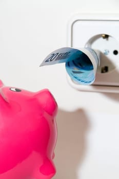 Close-up of a pink piggy bank in front of a socket with a 20-euro banknote plugged in.