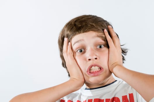 Ten-year-old boy presses his palms on his cheeks with an astonished expression against a white background.