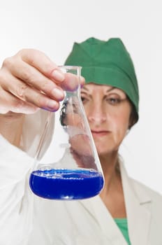 Laboratory technician holds a glass flask with blue liquid and controlling gaze.