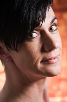 Side closeup of a middle-aged black-haired woman against an orange patterned background.