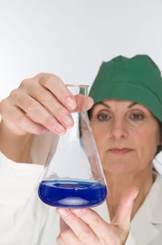 Laboratory technician holds a glass flask with blue liquid and controlling gaze.