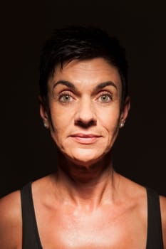 Head-and-shoulder portrait of a middle-aged black-haired woman against a black background looking into the camera in the spotlight.