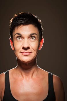 Head-and-shoulder portrait of a middle-aged black-haired woman against a black background looking upwards in the spotlight.