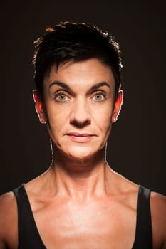 Head-and-shoulder portrait of a middle-aged black-haired woman against a black background looking into the camera in the spotlight.