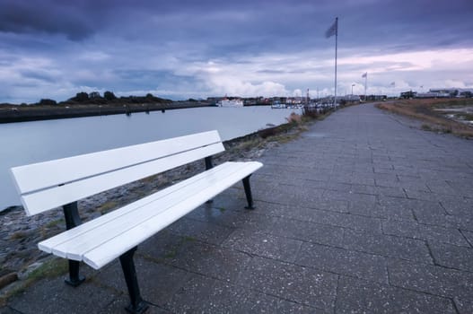 Wide-angle view of the harbour of Bensersiel in East Frisia with a white bench in the foreground at dusk