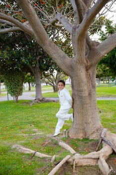 Young boy with white sailor suit leaning on a big tree in his First Communion