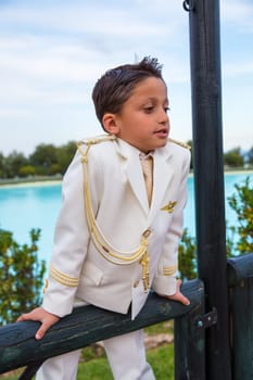 Young boy with white sailor suit leaning on a wooden fence in his First Communion