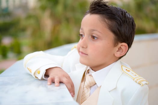 Young boy with white suit leaning on a wall in his First Communion. Shallow depth of field.