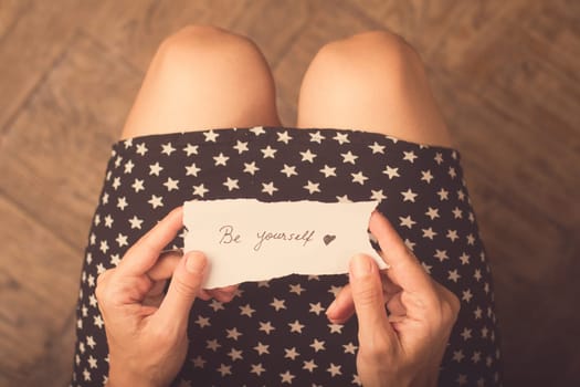 Woman with star patterned dress holding a note with be yourself message on it