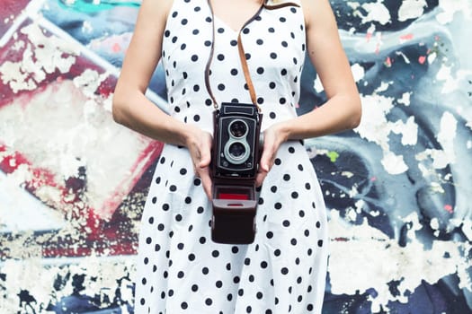 Horizontal view of a woman in dotted dress holding a camera against a graffiti wall
