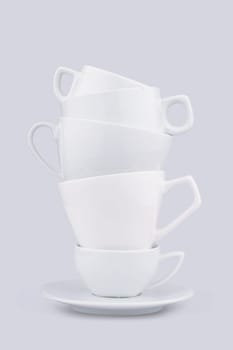 Front view of white ceramic coffee cups piled up on a dish on grey background