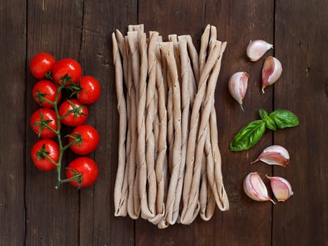 Raw italian pasta, basil and vegetables on wooden background