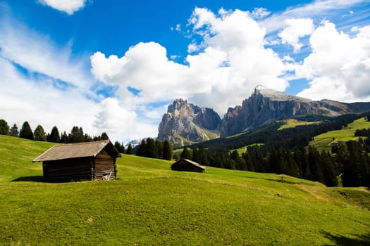panoramic view of the Seiser Alm in a sunny day with blue sky and clouds with refuge in foreground and mountain range in the background