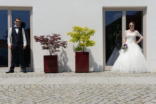 Happy young bridal couple with sunglasses in front of an old house