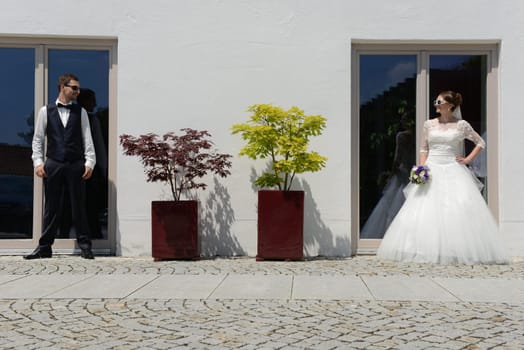 Happy young bridal couple with sunglasses in front of an old house