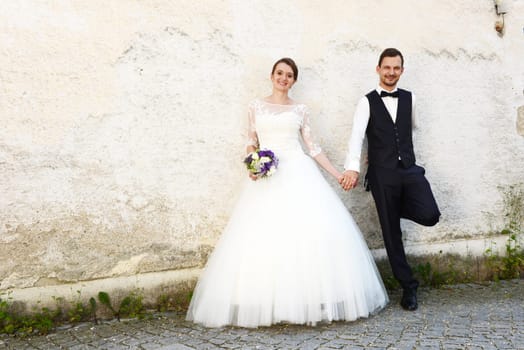 Happy young bridal couple in front of an old house wall