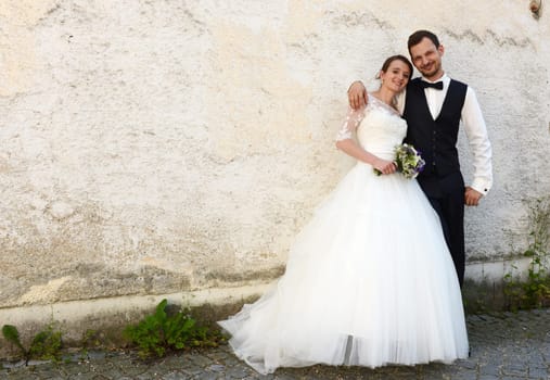 Happy young bridal couple in front of an old house wall