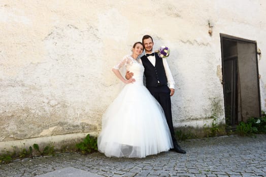 Happy young bridal couple in front of an old house wall