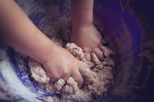 Top view of child hands working the bread dough in a plastic colored pot