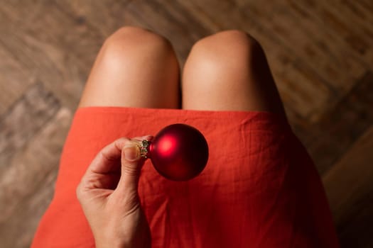 Top view of woman with red dress holding one red Christmas globe above her knees