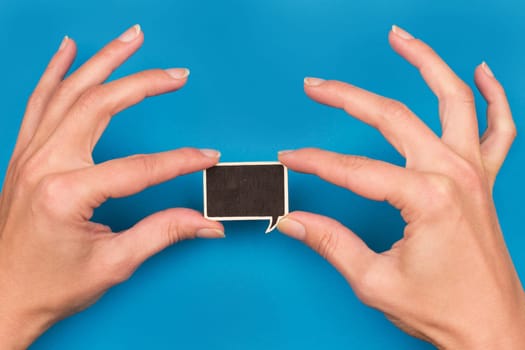 top view of two hands holding a wooden speech bubble on blue background, concept for communication