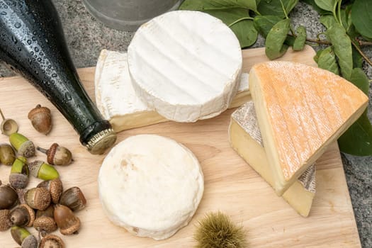 wooden tray with different french cheeses and bottle of cider