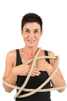 Frontal upper body view of a black-haired middle-aged woman with rope placed around her body against a white background looking dissatisfied into the camera.