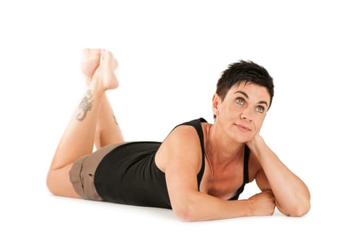 Full-body view of a black-haired middle-aged woman barefoot in shorts and black top lying on her stomach against a white background looking dreamily upwards.