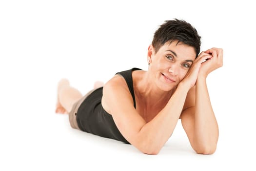 Full-body view of a black-haired middle-aged woman barefoot in shorts and black top lying on her stomach against a white background looking into the camera.