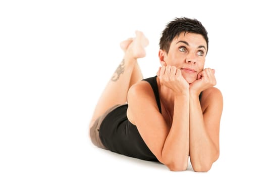 Full-body view of a black-haired middle-aged woman barefoot in shorts and black top lying on her stomach against a white background looking dreamily upwards.