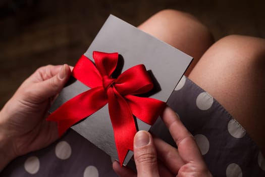 Close up of the hands of a woman with polka dress holding a black card with red ribbon above knees