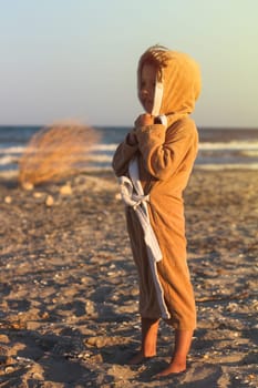 vertical portrait of young girl in brown towel cloth standing on the beach by the seaside