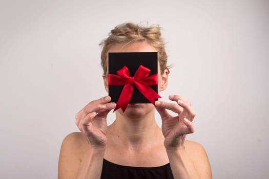 Portrait of a young Caucasian woman holding a black gift card with red ribbon in front of her face