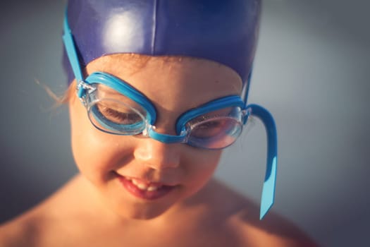 swimmer girl portrait with blue cap and swimming glasses looking down and smiling