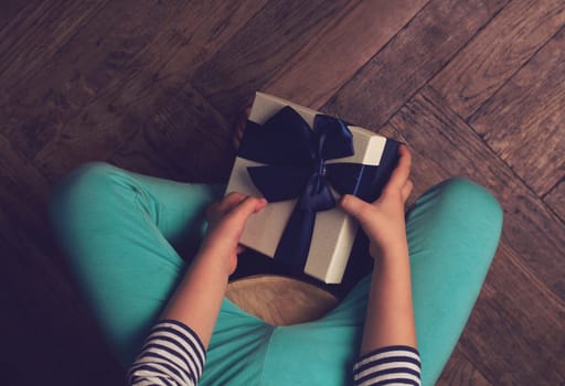 Top view of kid with blue pants and stripes sweater holding a gift box with ribbon in his hands