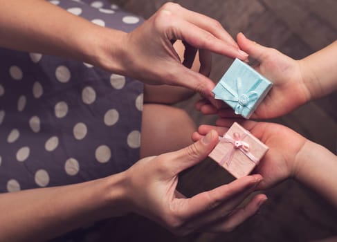 Top view of hands of woman giving two pink and blue small gift boxes to her kid with open hand