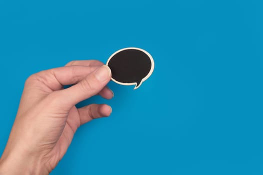top view of hand holding a black wooden speech bubble on blue background