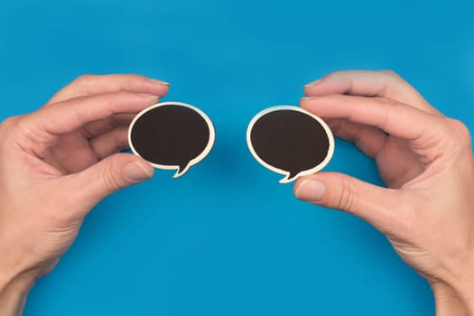 top view of hands holding two black wooden speech bubbles on blue background