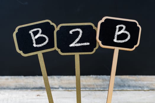 Business acronym B2B as Business To Business written with chalk on wooden mini blackboard labels, defocused chalkboard and wood table in background