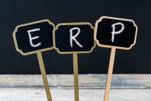 Business acronym ERP as Enterprise Resource Planning written with chalk on wooden mini blackboard labels, defocused chalkboard and wood table in background