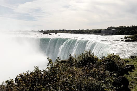 A view of the Niagara falls on the Canadian site with the river flowing.over the edge and the mist coming up..