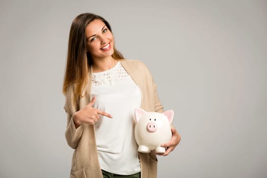 Beautiful and happy woman holding a piggy bank and making thumb up